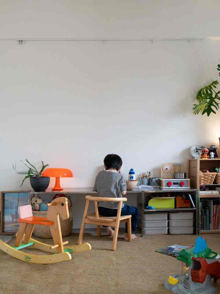 ナチュラルな木目調と白い壁の子供部屋、机に座る子供とおもちゃや収納が配置された温かみのあるインテリア