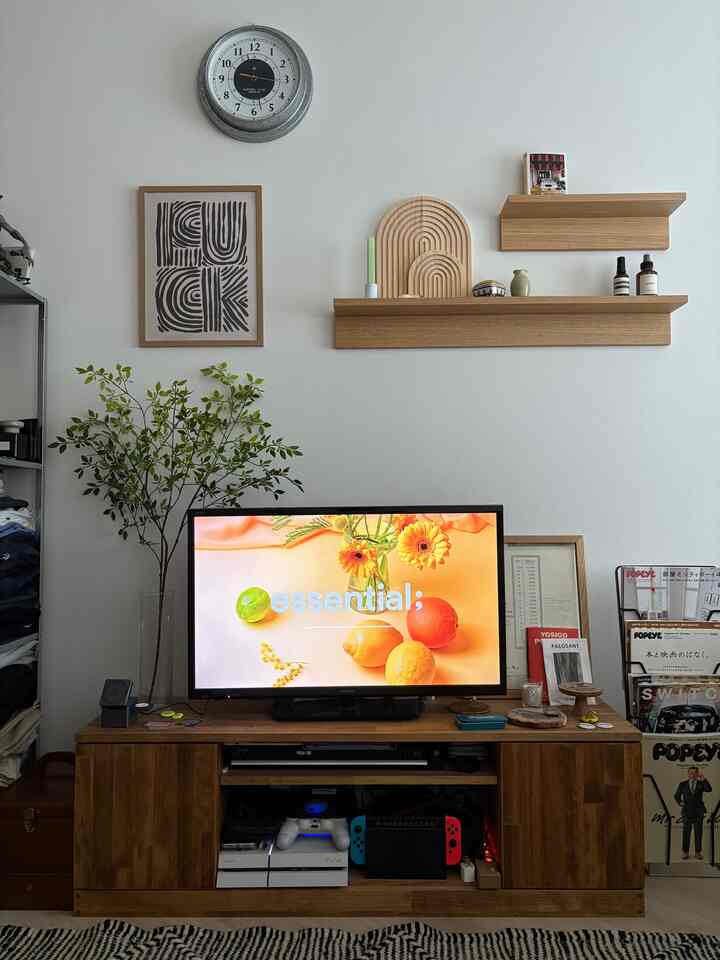 ナチュラルな木目調と白い壁のリビング、壁棚とテレビ台に植物や飾りが配置された雰囲気のある空間