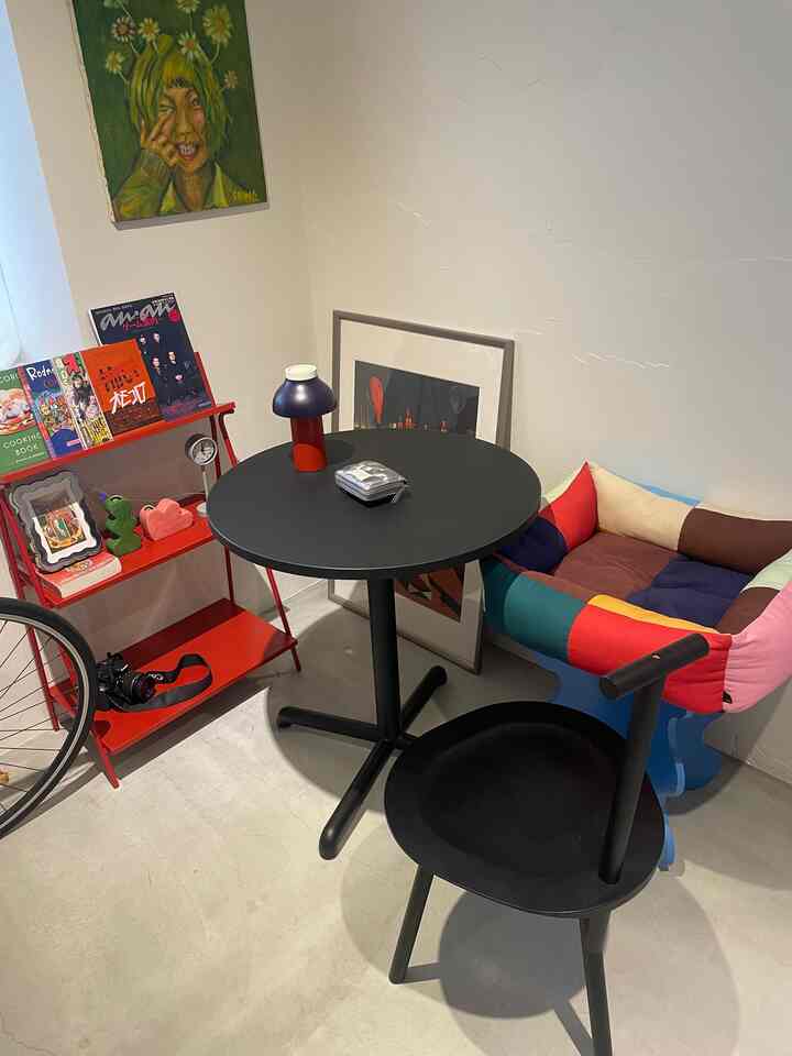 黒と赤のトーンの小さな部屋、丸い黒いテーブルとカラフルなアームチェア、赤い本棚が配された雰囲気のあるインテリア