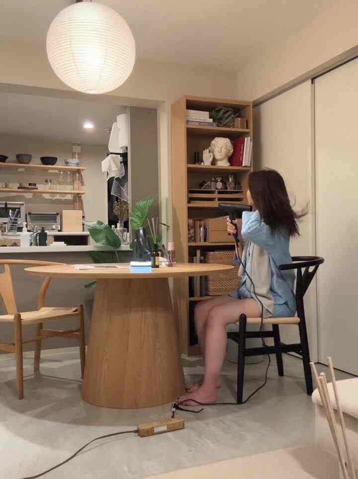 Natural color simple modern living and dining space featuring a wooden dining table, chairs, pendant light, and bookshelf with a cozy atmosphere