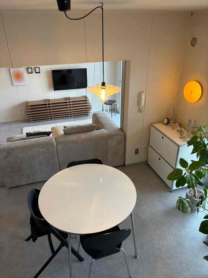 白とグレーのトーンのリビング兼ダイニングスペース、丸いダイニングテーブルとグレーのソファ、ペンダントライトが配置された落ち着いたミニマルな雰囲気のインテリア