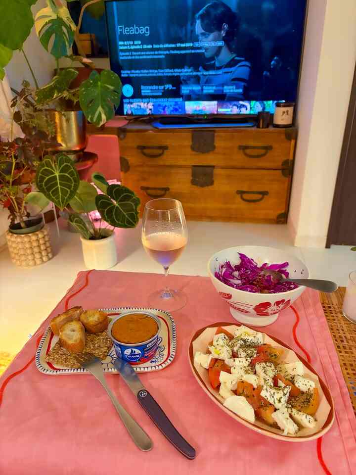 Cozy living room with pink tablecloth featuring single-person dining setup with wine glass and simple dishes, alongside lush green plants