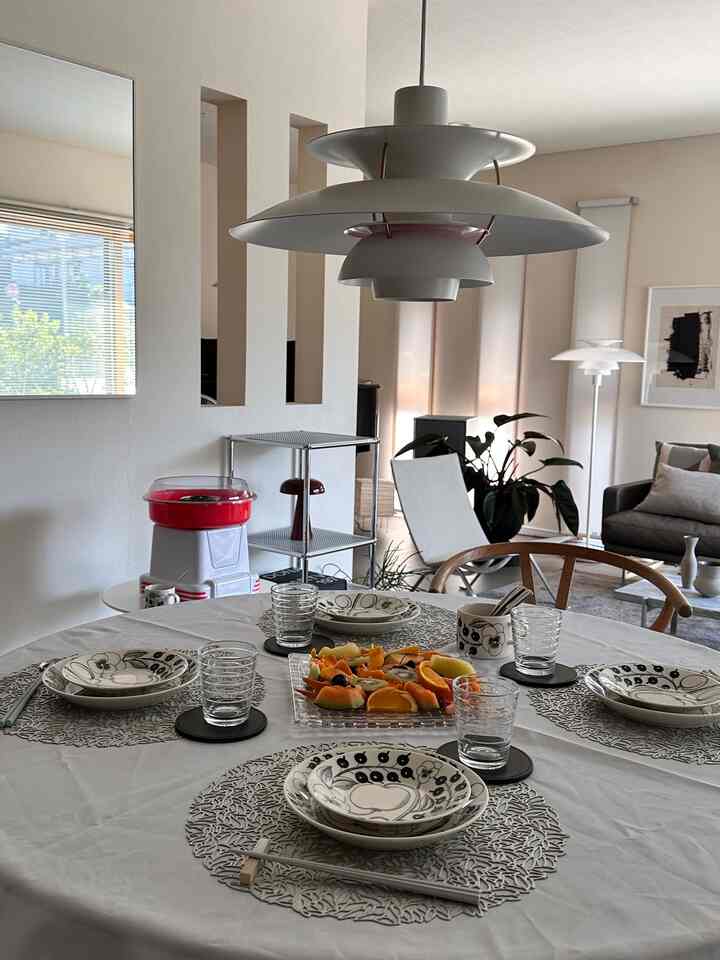 白と茶色のトーンのダイニング、丸い食卓と食器、ペンダントライトが配置された雰囲気のある空間