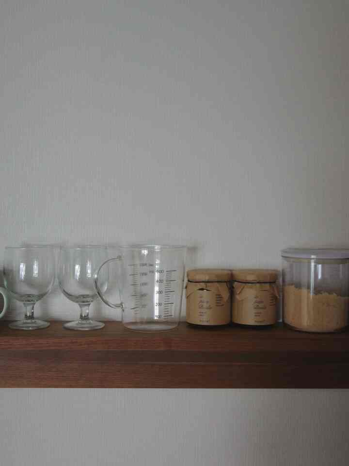 ナチュラルな白い壁と木目調の棚にガラスや計量カップが配置されたキッチンの印象的な空間