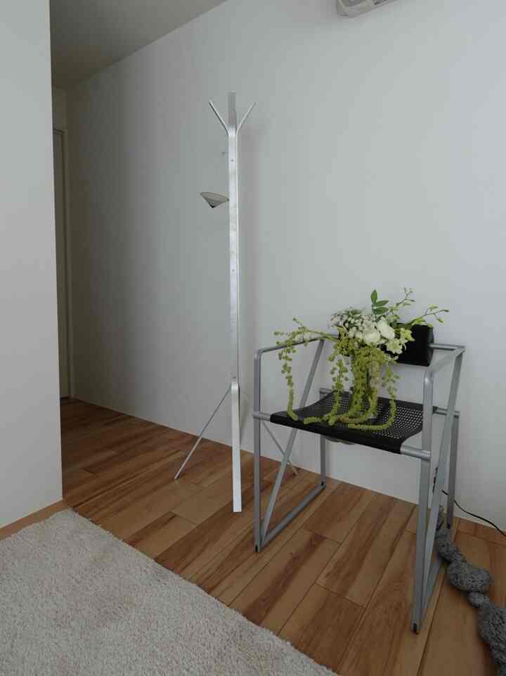 白い壁と木目調の床が調和するミニマルな玄関スペース、金属製のコートハンガーとアームチェアが配置されている。