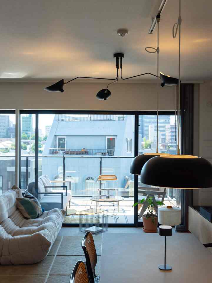 白とナチュラルカラーのリビング、ベージュのソファとネイビーのクッション、ペンダントライトが配置されたモダンな空間