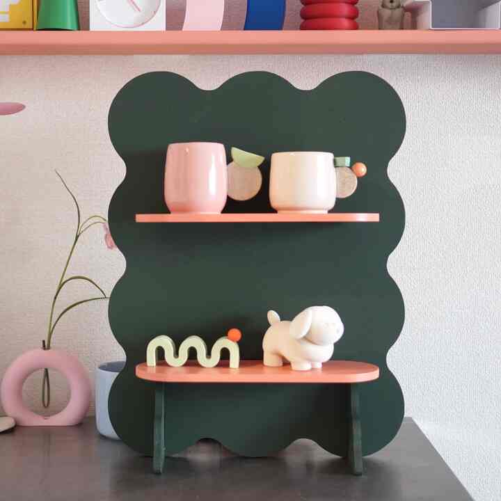 A pink and green toned shelf displaying mugs and decorative objets in a stylish interior setup