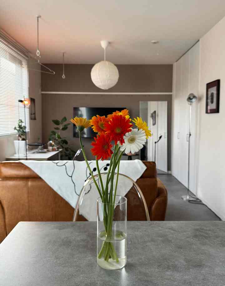 グレー調のテーブルとブラウンのレザーソファが配置されたモダンでナチュラルなリビング、中央に透明なガラス花瓶と色とりどりの切り花が置かれている印象的な空間
