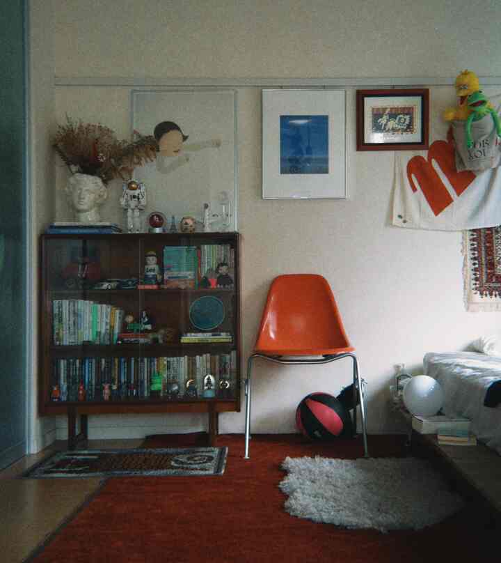 赤とオレンジのトーンが映える1LDKリビング、ミッドセンチュリーモダンのオレンジチェアや多彩なオブジェが配置された温かみのある空間