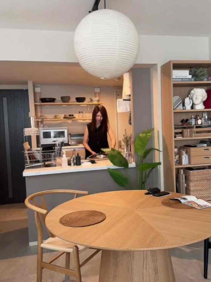 白い天井とナチュラルな木目調のダイニングテーブルと椅子、本棚が配置されたモダンなダイニングルームとキッチン