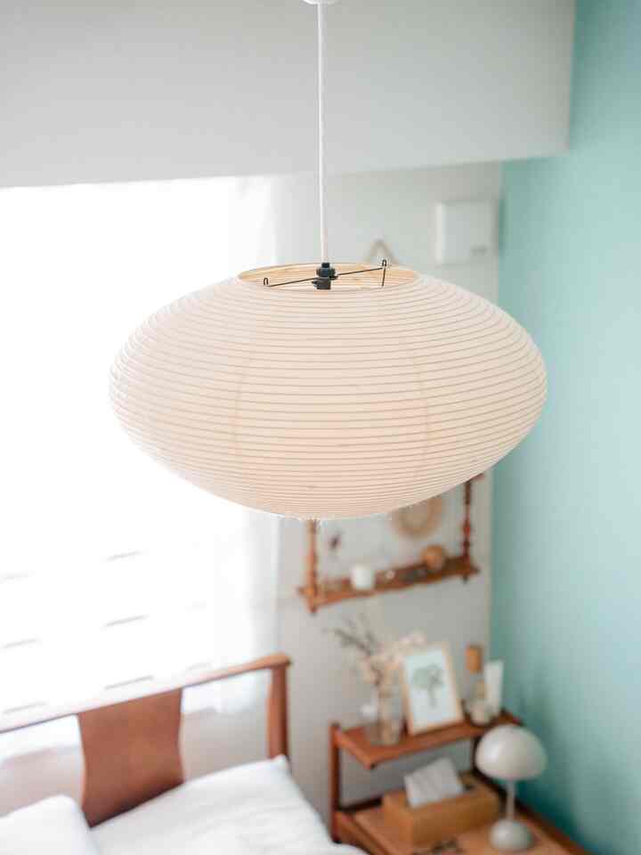 A bedroom in natural tones featuring a softly curved pendant light centrally hung, creating a calm and cozy atmosphere