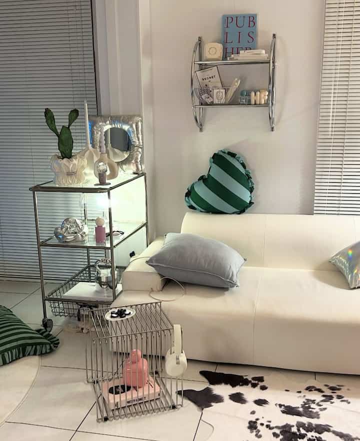 白と緑を基調としたリビング、白いソファと緑のストライプクッション、メタルシェルフとケージが配置されたモダンで印象的な空間