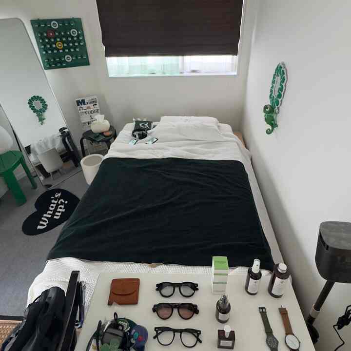 Small bedroom with white walls and green accents, featuring a neatly arranged bed and desk