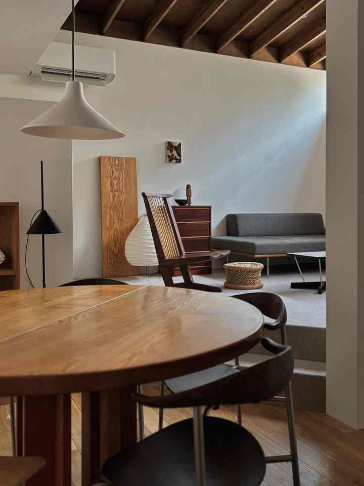 A modern living and dining room in natural and white tones, featuring wooden furniture, armchair, and floor lamps in a serene space