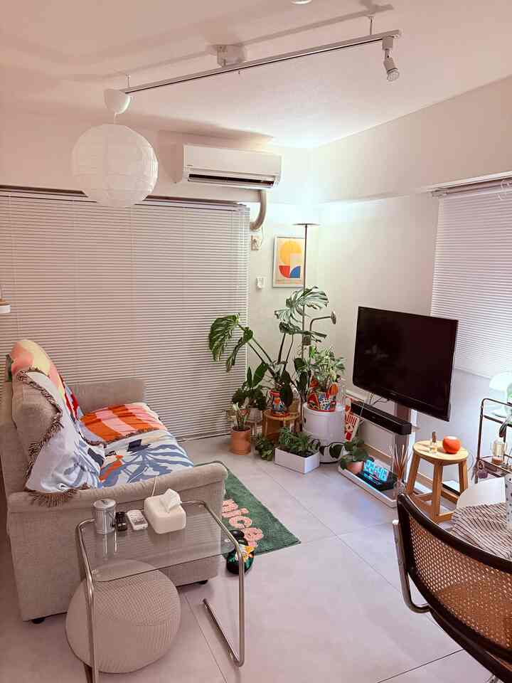 明るくナチュラルな白色調のリビング、透明なガラステーブルと多彩な植物が配置されたミニマルな空間