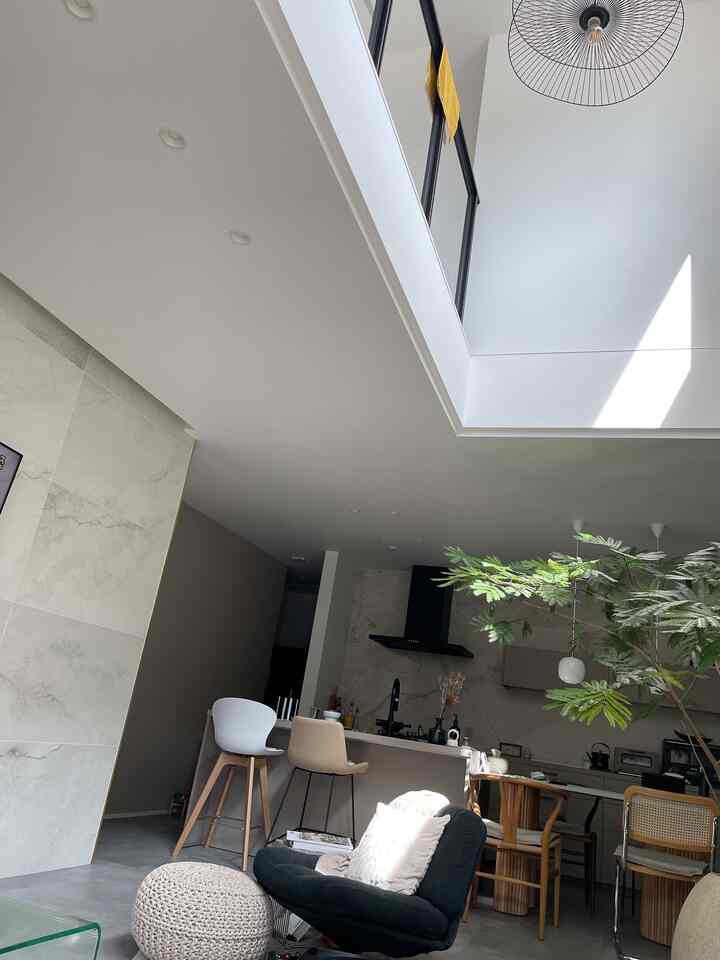 明るいホワイトと木目調が調和したキッチンとリビング、アームチェアとバースツールが配置された開放的なインテリア