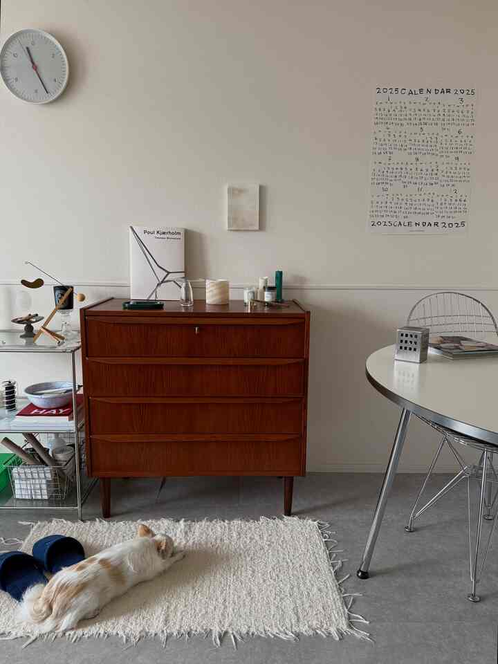 白と茶色のトーンのリビング、ヴィンテージの木製チェストと丸テーブル、犬が横たわるナチュラルな雰囲気のインテリア