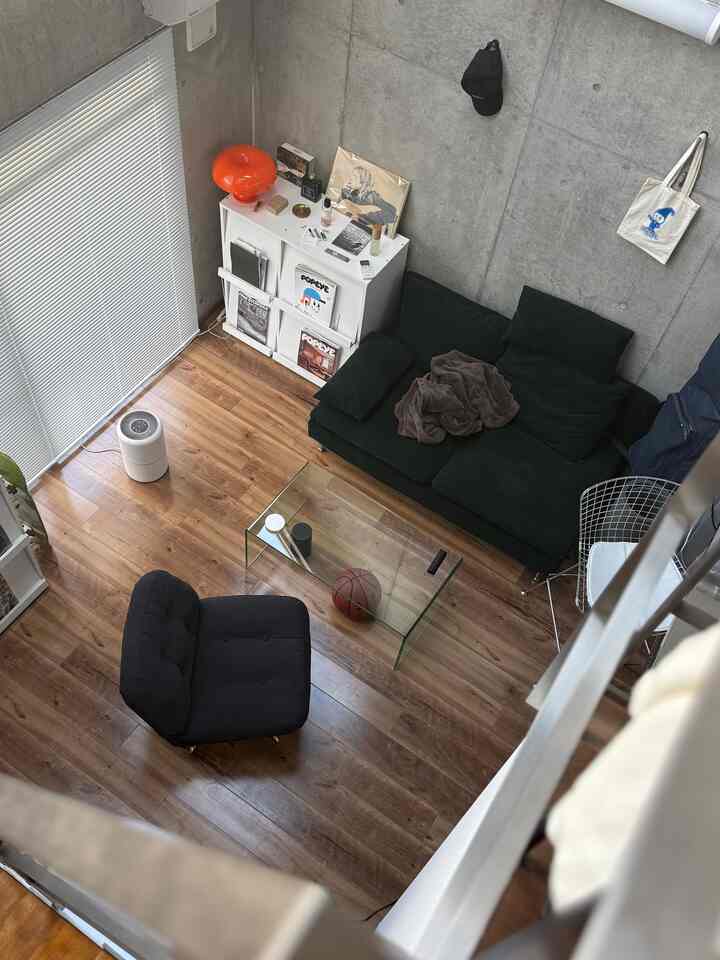 Modern living room with natural wood flooring, black sofa, and transparent glass table