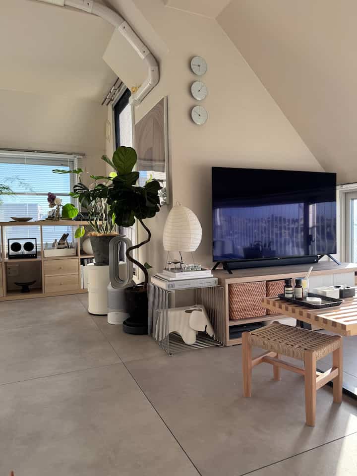 明るいホワイトと木目調が調和した北欧風リビング、大型テレビとフロアランプ、観葉植物が配置された雰囲気のある空間