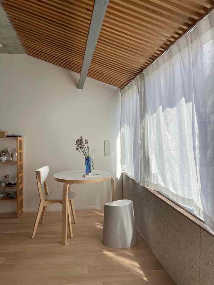 白と木目調が調和したワンルームのダイニングスペース、窓からの明るい自然光とシンプルな花瓶が配置された雰囲気のあるインテリア