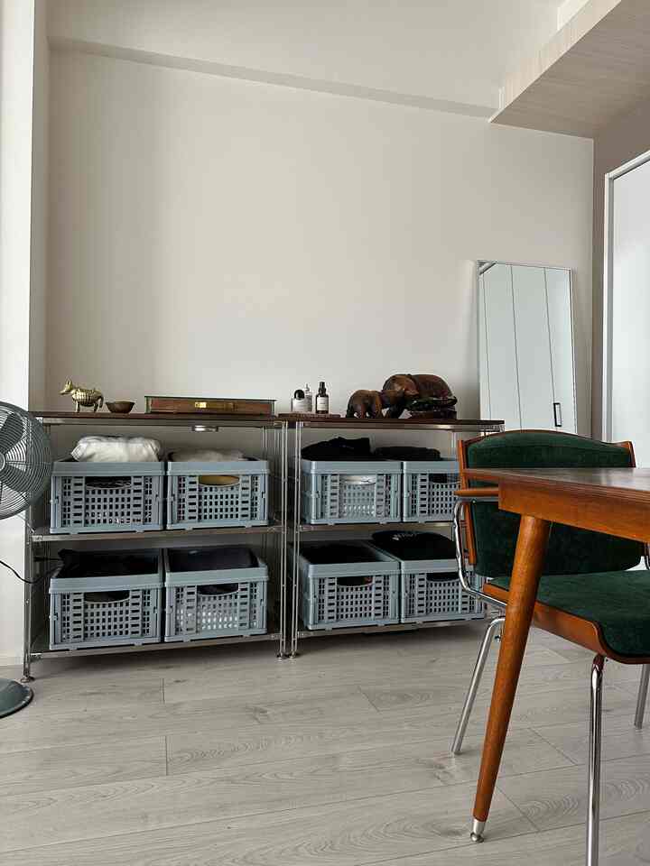 ライトグレーの床とシェルフが配置されたリビング兼ダイニング空間、木目調のテーブルとアームチェアが置かれたモダンで整ったインテリア