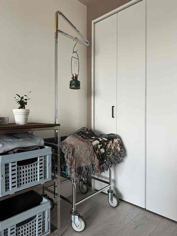 白い壁とグレーの床、メタルシェルフと青いバスケット、緑のLEDランタンと観葉植物がある実用的な収納スペース