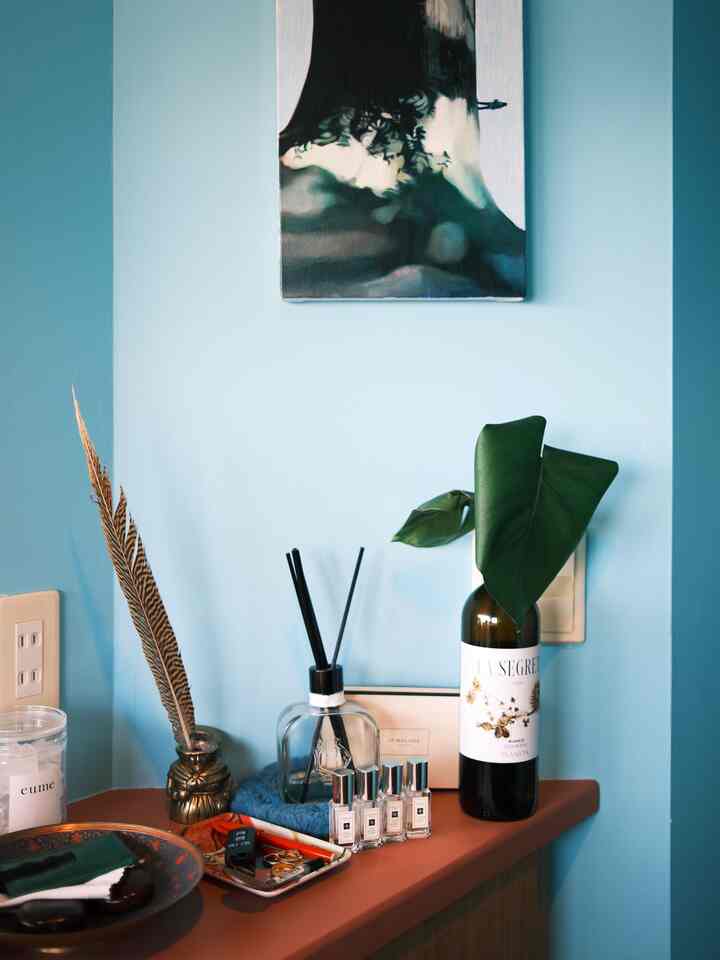 明るい青い壁と木目調家具がある玄関、ディフューザーと絵が配置された雰囲気のあるインテリア