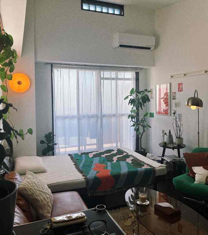 Natural green and brown toned 1K bedroom featuring plants and mid-century modern furniture with a cozy atmosphere