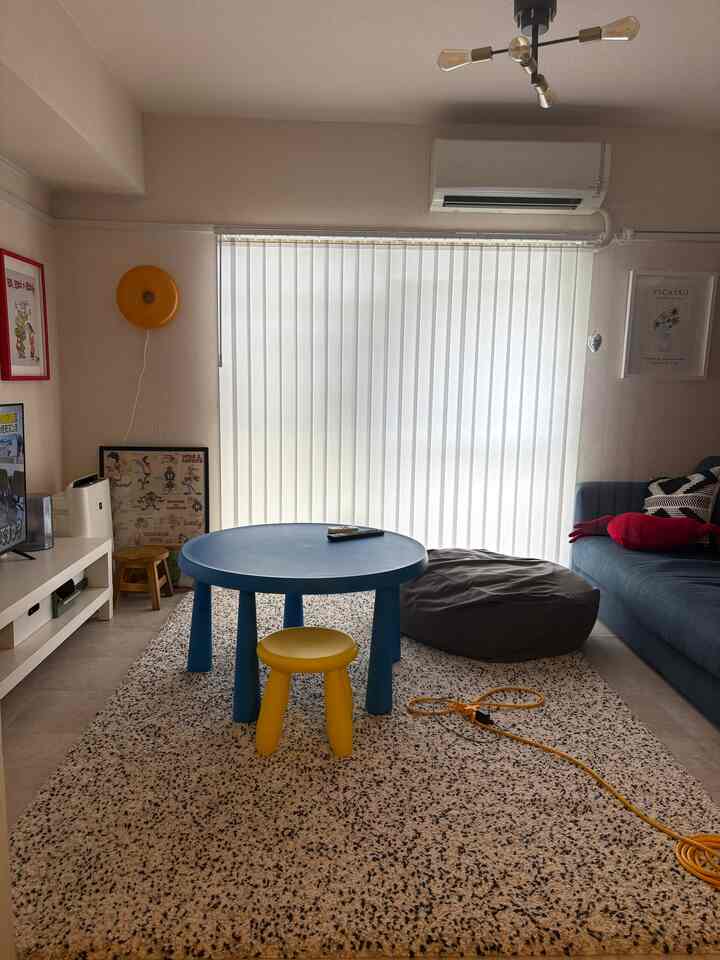 Sky blue round table and yellow stool in a living room featuring white vertical blinds and a plush rug in an American interior style.