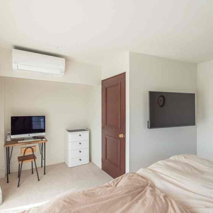 White and brown toned bedroom featuring a desk, dresser, and mounted TV in a simple modern space