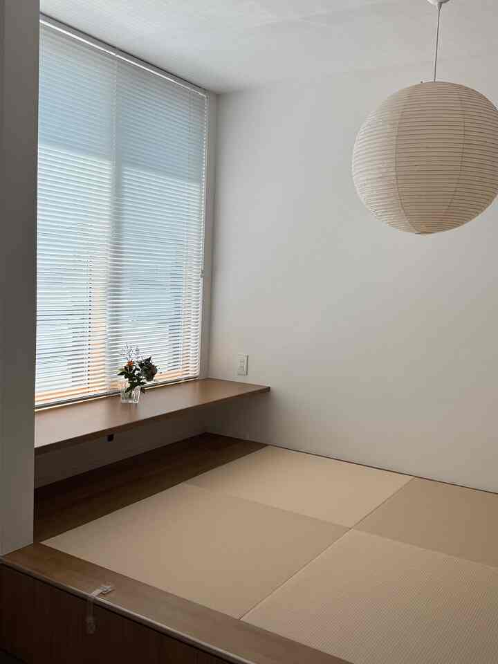 自然なベージュと木目調の畳の部屋、窓辺の棚とアカリのペンダントライトが配置された印象的な和モダン空間