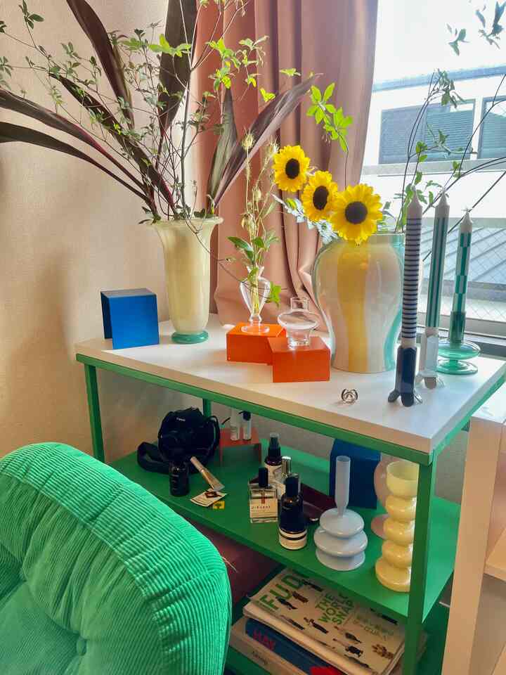 パステルカラーとカラフルな色調の1LDKリビング、花瓶とキャンドルが置かれたプラッツァ棚と緑のソファが配置された印象的な空間