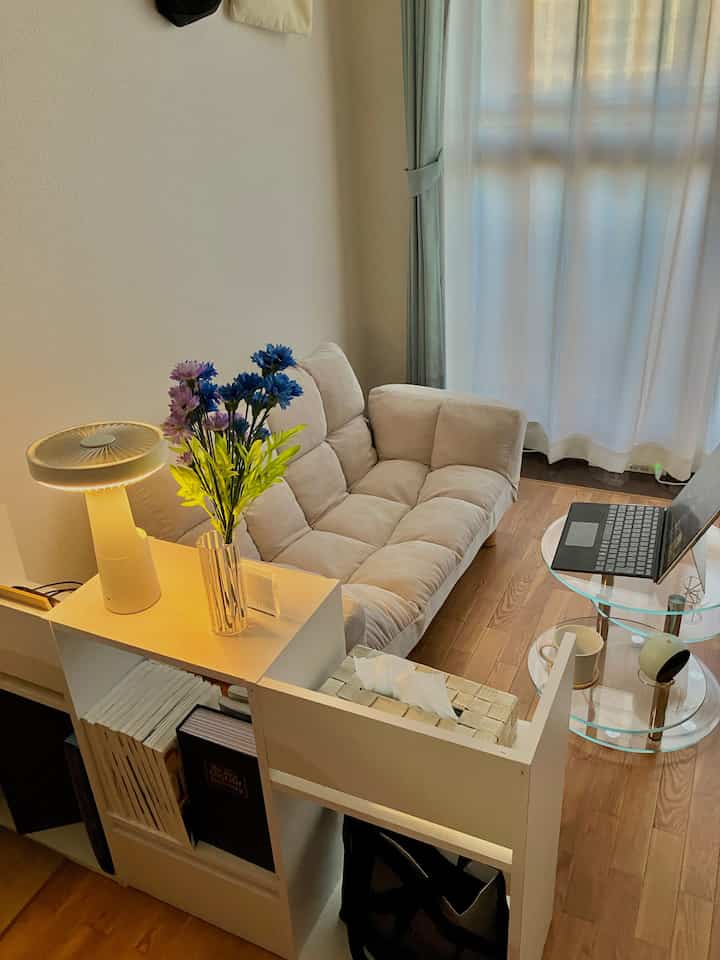 Compact living room with white walls and brown wooden floor, featuring beige two-seater recliner sofa and glass side table, creating a cozy atmosphere