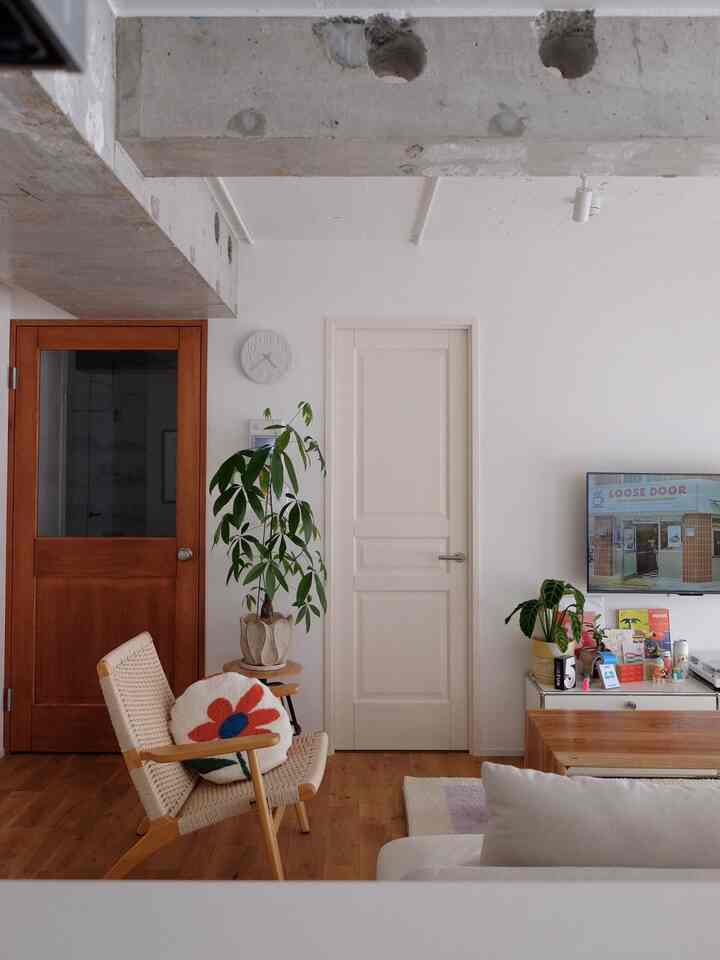 White-walled living room with wood tone flooring, featuring green plants, natural armchair, and sofa creating a cozy atmosphere
