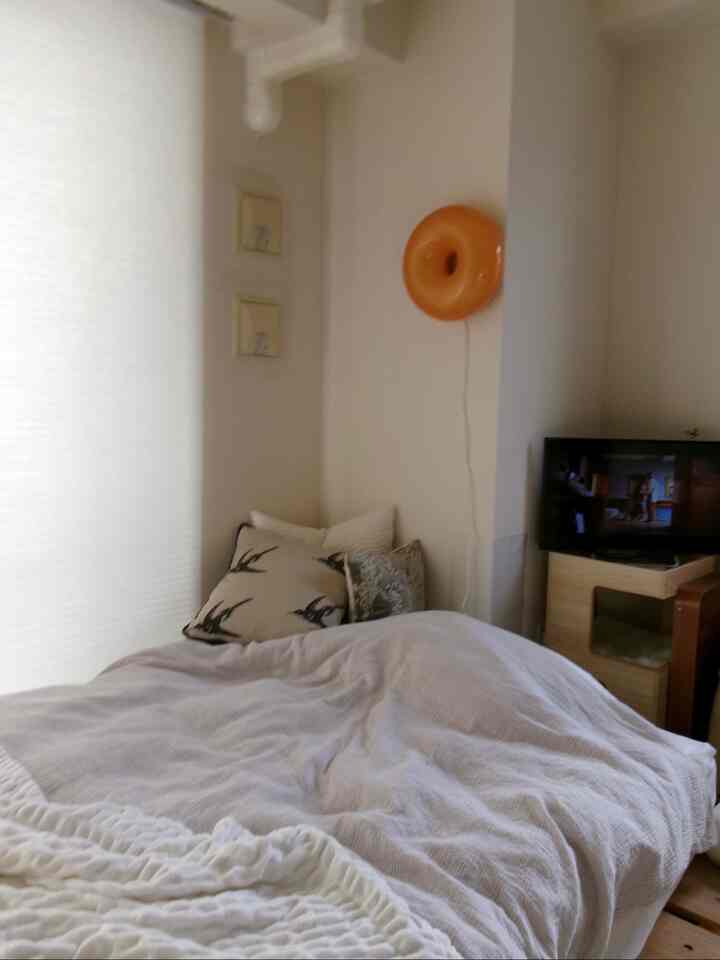 ベージュとホワイトのトーンの寝室、ベッドとクッション、オレンジ色の壁ライトが配置された温かみのあるインテリア