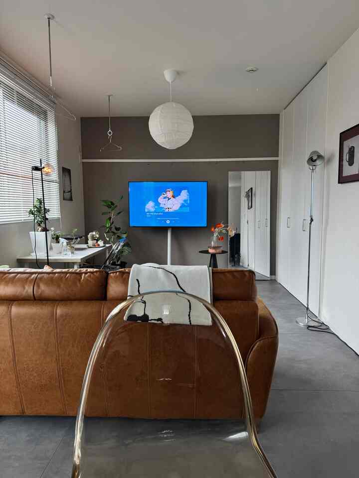 A gray and brown toned living room featuring a transparent chair, sofa, and TV stand in a simple modern space