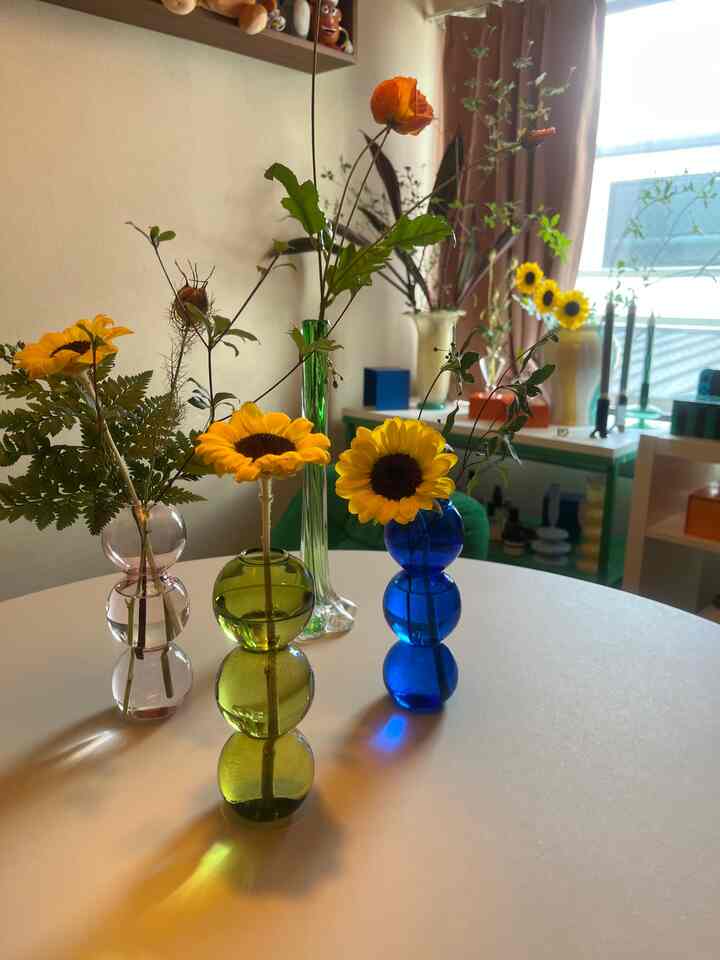 ミッドセンチュリーモダンスタイルの1LDKリビング、白いテーブルにカラフルな花瓶とひまわりが置かれた雰囲気のあるインテリア