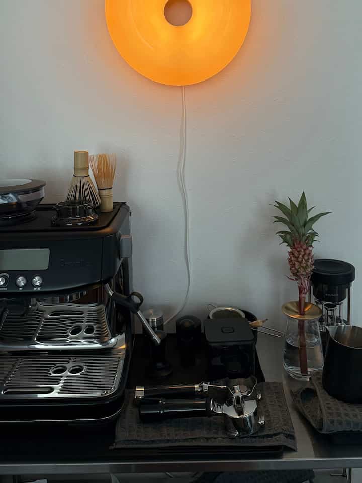 白い壁と黒いコーヒーマシンがあるリビングのバーカウンター、暖かな照明が印象的な空間