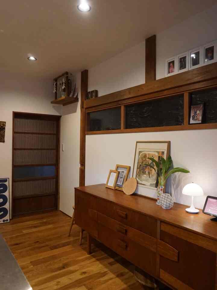 A natural-tone kitchen-adjacent space featuring a brown wood sideboard, white walls, table lamp, and traditional old folk house style