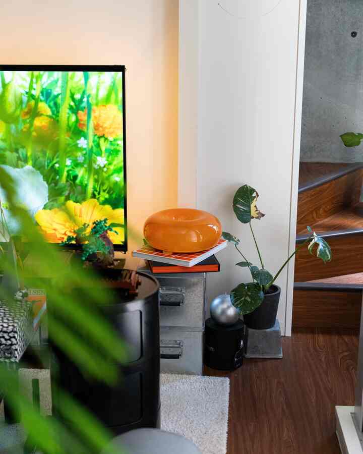 Living room corner with white walls and dark brown wooden floor, featuring mid-century modern furniture and plants in a cozy atmosphere