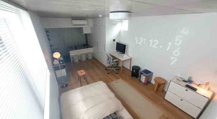 White and wood-toned studio bedroom and home office space featuring minimal furniture with a simple interior design