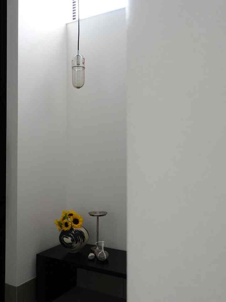 白い色調の小さな玄関、黒いベンチとペンダントライトが配置されたシンプルなインテリア