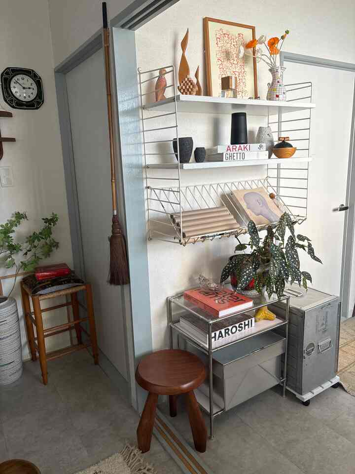 ナチュラルな色調の廊下の一角に、金属製の収納棚と木製のスツール、壁掛け時計が配置された落ち着いた雰囲気のインテリア