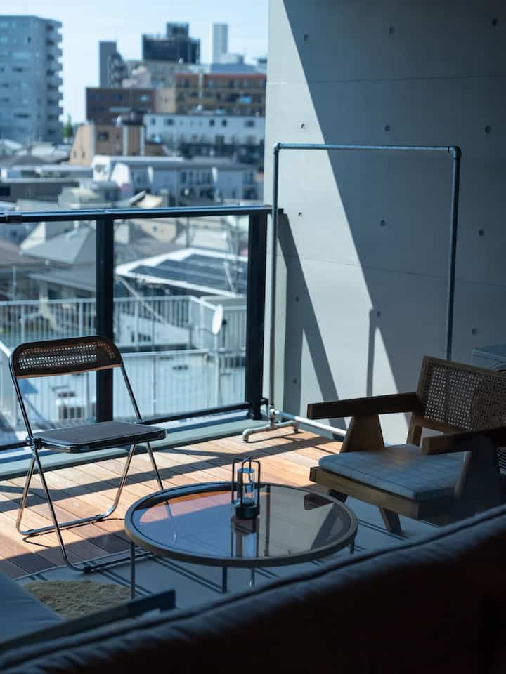 ナチュラルトーンのバルコニー、木製のアームチェアとガラスのコーヒーテーブルが配置された落ち着いた屋外空間