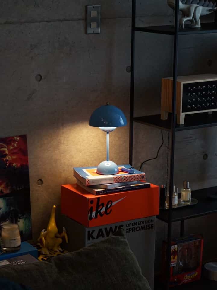 グレーのコンクリート壁と黒いメタル棚があるモダンな一人暮らし空間、青いランプとアートトイが特徴の印象的なインテリア