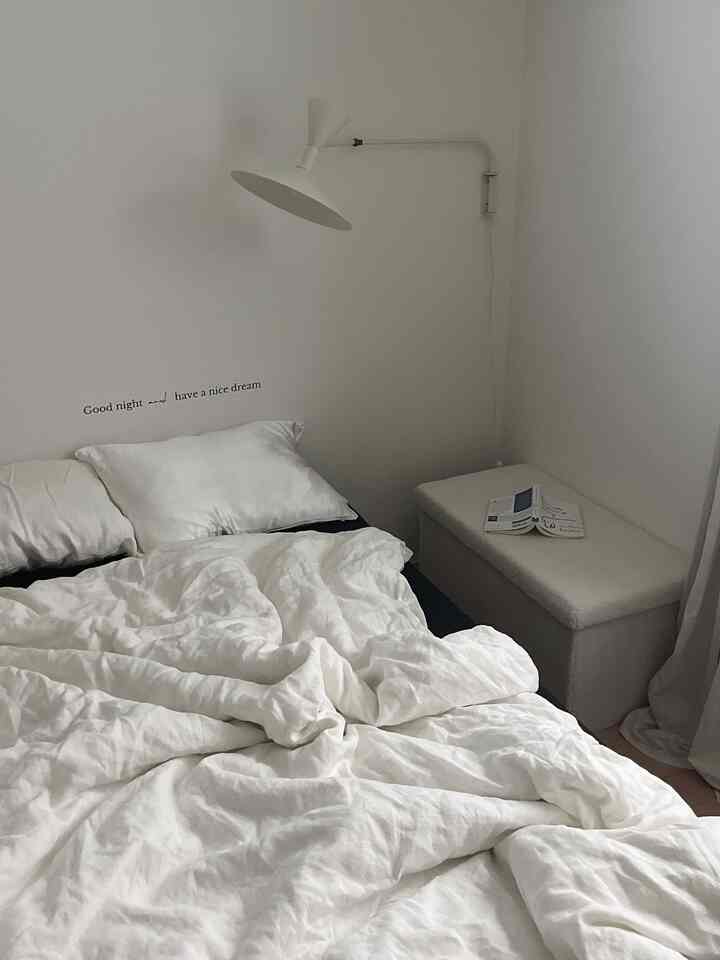 Soft beige and ivory tone bedroom featuring white bed with duvet cover and pillows, wall sconce lighting creating a cozy atmosphere