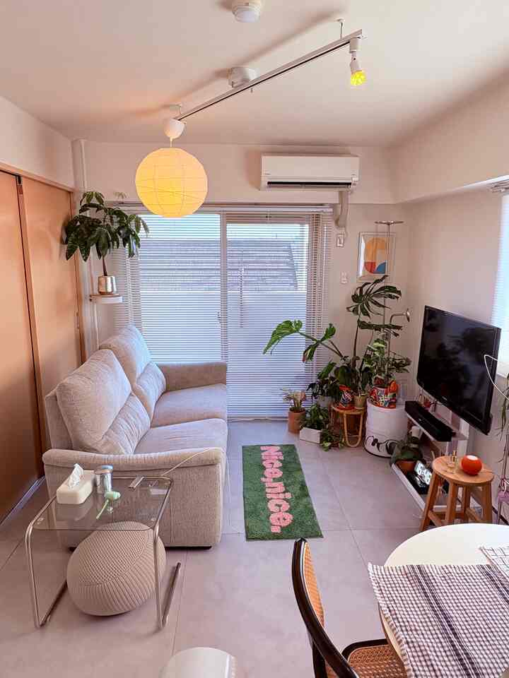 明るい色調のリビング、ベージュのソファとダイニングテーブル、多彩な観葉植物が調和するモダンな空間