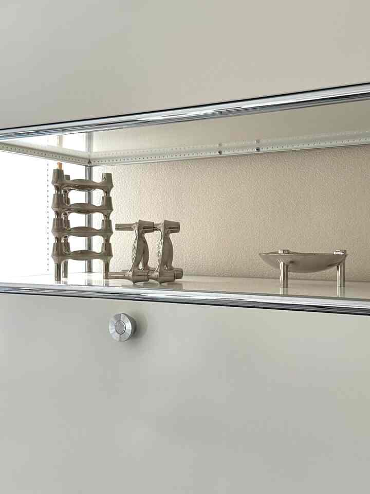 ホワイトとシルバーのトーンで構成されたモダンな壁掛けシェルフに銀色のオブジェが並ぶミニマルなインテリア