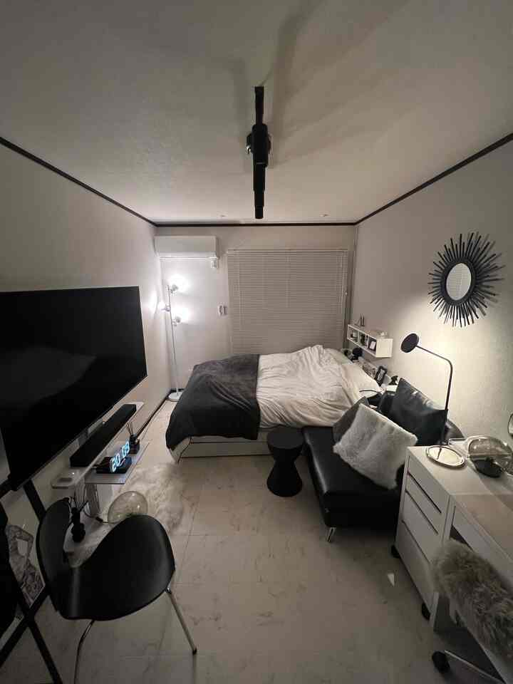 白と黒のモノトーンが調和したシンプルなワンルーム寝室、白いブラインドと黒いソファが配置された雰囲気のある空間