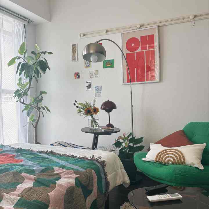 白い壁の8畳のミッドセンチュリーモダンな一人暮らしの部屋、緑色のアームチェアと大きな植物、ベッドが配置された印象的な空間